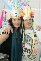 A young person with a brightly coloured feather headress standing next to a laday with her arm around them smiling.