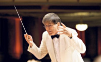 Hialry is photographed in a white suite he is holding a baton in mid air conducting