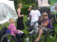 Two young women who are wheelchair user's sitting outside on the grass with tent like structures behind