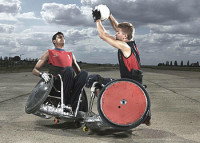 Photograph showing two wheelchair rugby players. On has the ball the other is challenging him.