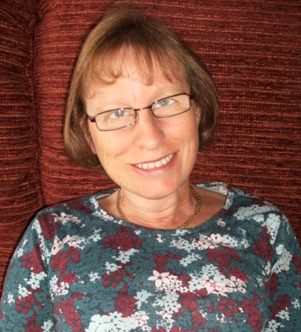 This is a portrait photo of Liz Porter. She's smiling, and looking at the camera. She is wearing a grey, red and white patterned top and glasses.